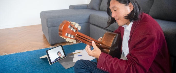 A man teaching guitar lessons online to his student